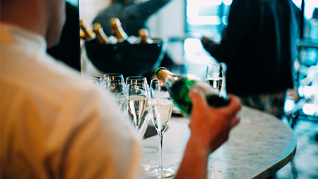 Over shoulder photo of bar tender pouring champagne in glasses on bar